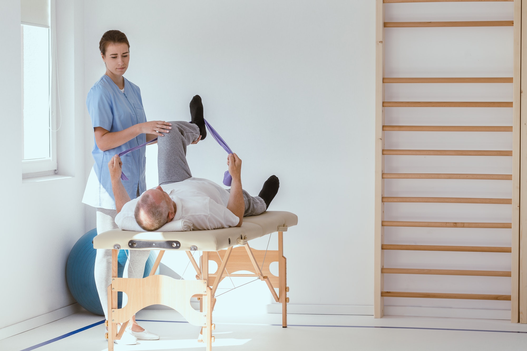 Injured patient lying on a physiotherapy bed and performing exercises with tapes