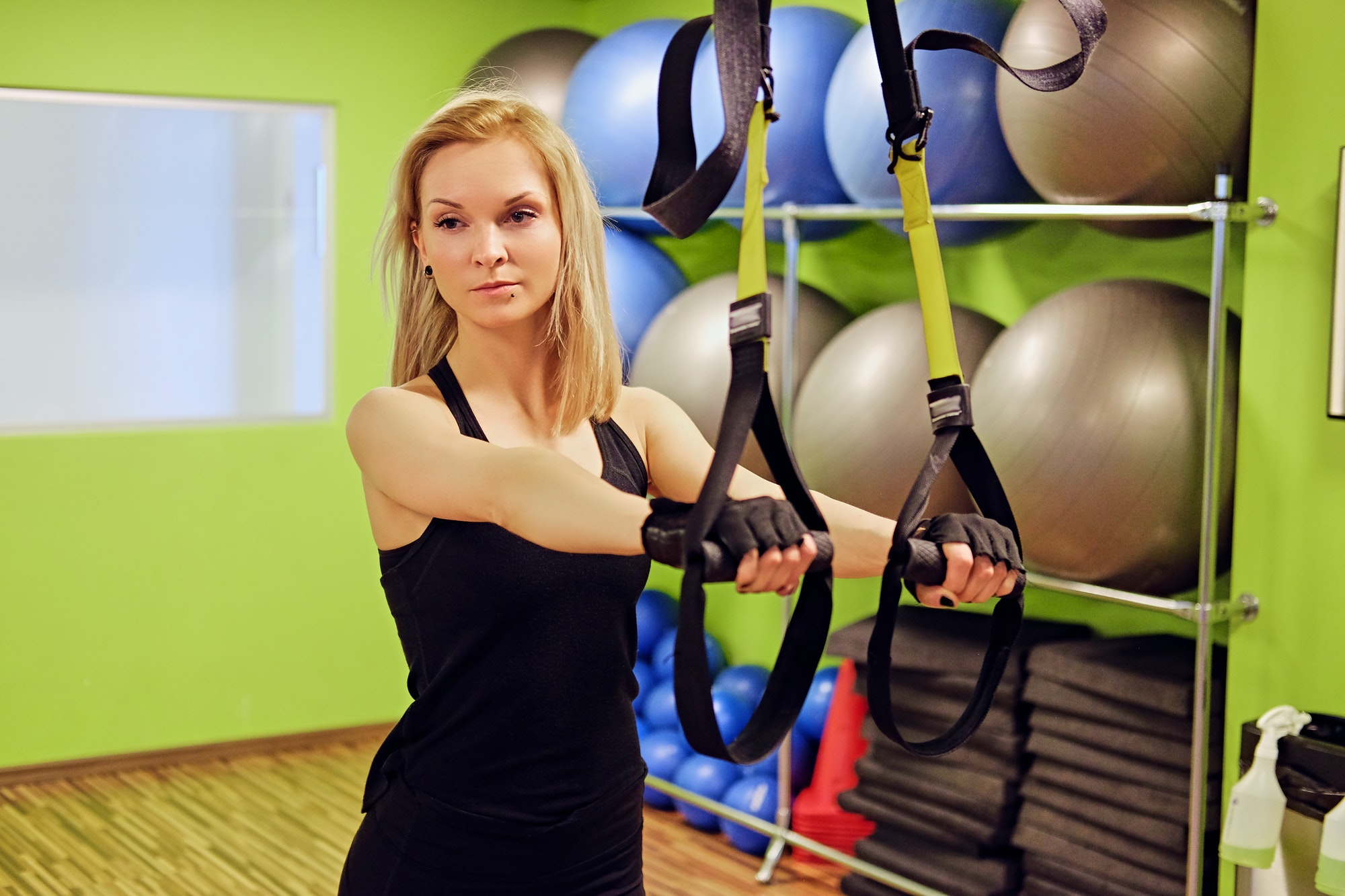Slim female doing trx straps exercises in a gym.